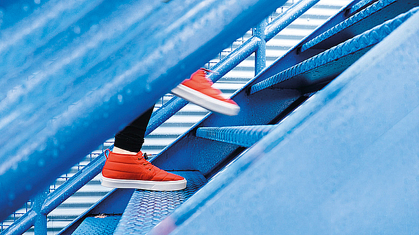 Nahaufnahme von Person mit orangen Schuhen, die eine blaue Treppe hinaufsteigt