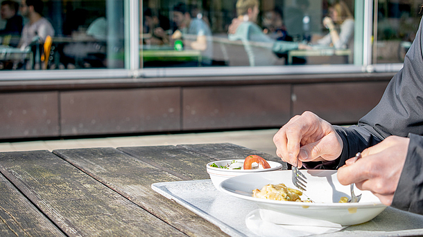 Eine Person mit Mensaessen vor der Kantine am Conti-Campus