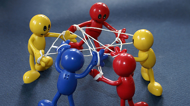 Fünf bunte Spielzeugfiguren stehen im Kreis und sind mit einem Faden "vernetzt"