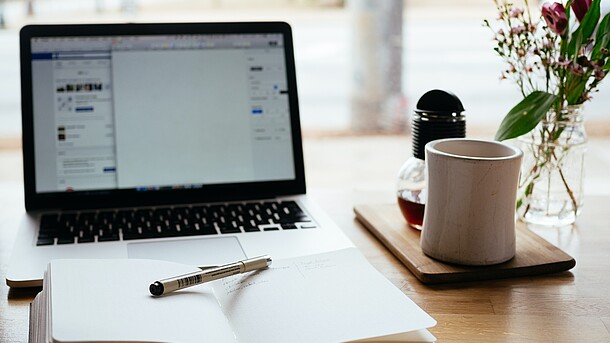 Tisch mit Notizbuch, Laptop und Kaffeebecher