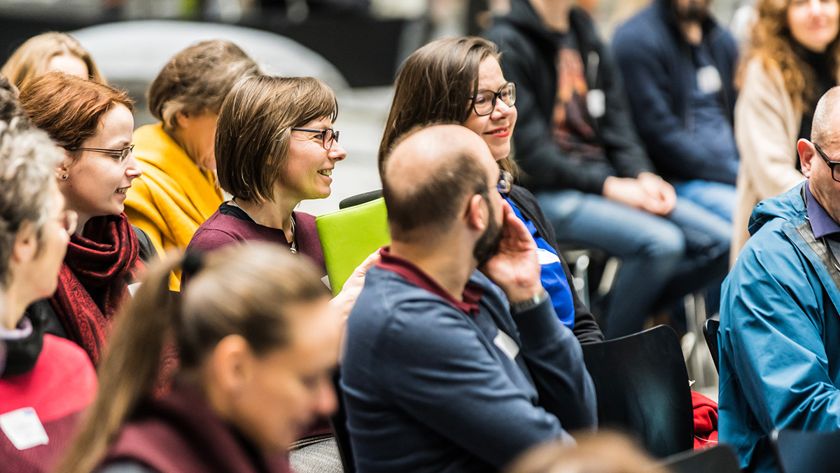 Eine Gruppe von Personen folgt im Plenum einem Vortrag im Lichthof.