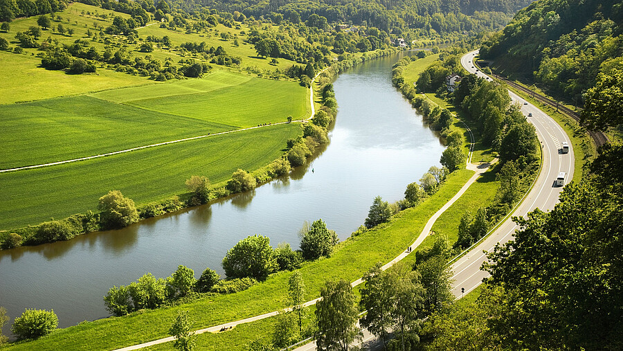 Ein Fluss, der durch eine sehr grüne Landschaft verläuft und parallel zu ihm ist eine Straße.