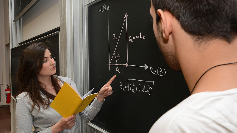 A woman explains a math problem on the blackboard to a man.